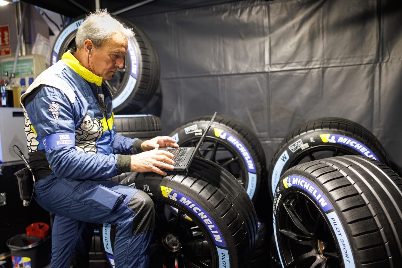 Technicien Michelin en combinaison travaillant sur un ordinateur portable au milieu de pneus de compétition